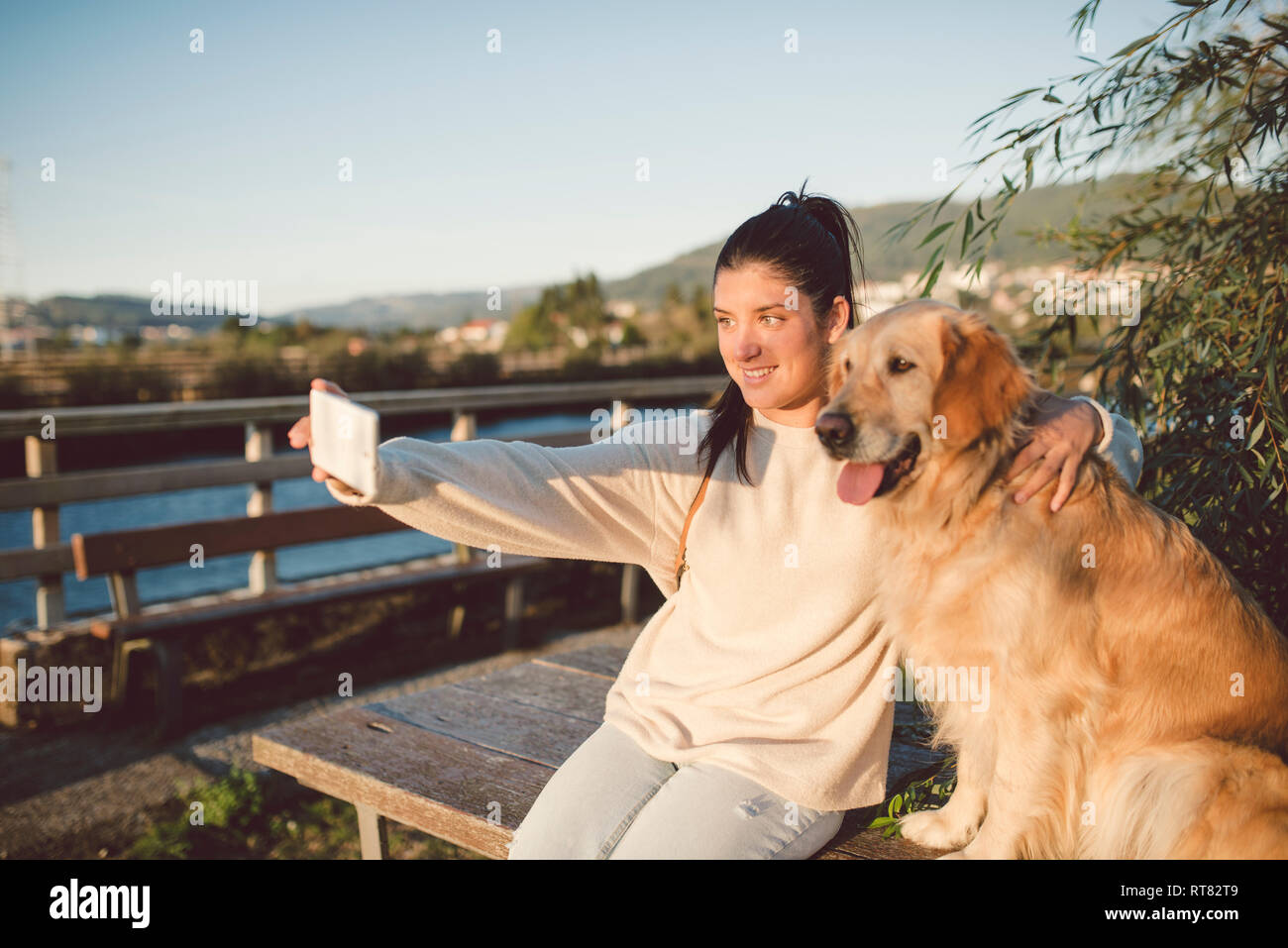 Smiling young woman taking a selfie with her dog at the waterfront ...