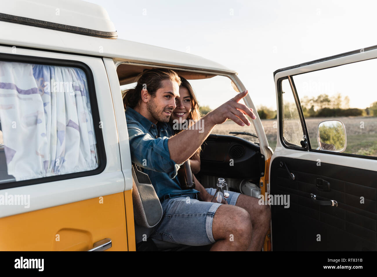 Happy couple sitting in their camper, man pointing at distance Stock Photo