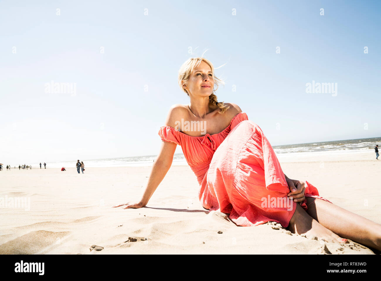 Woman in dress sitting on the beach Stock Photo - Alamy
