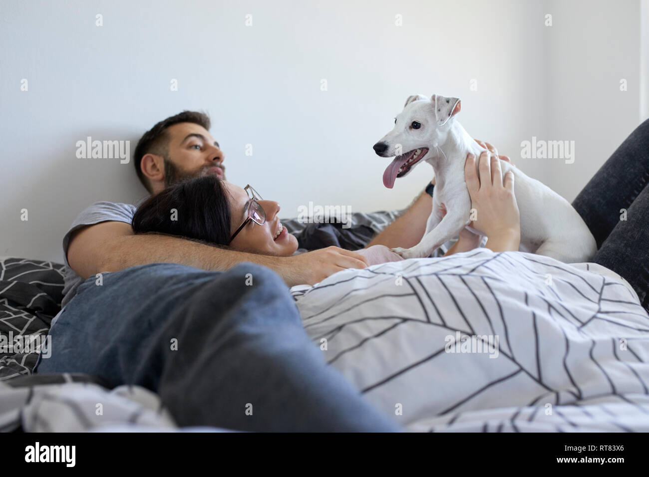 Couple lying on bed cuddling dog Stock Photo
