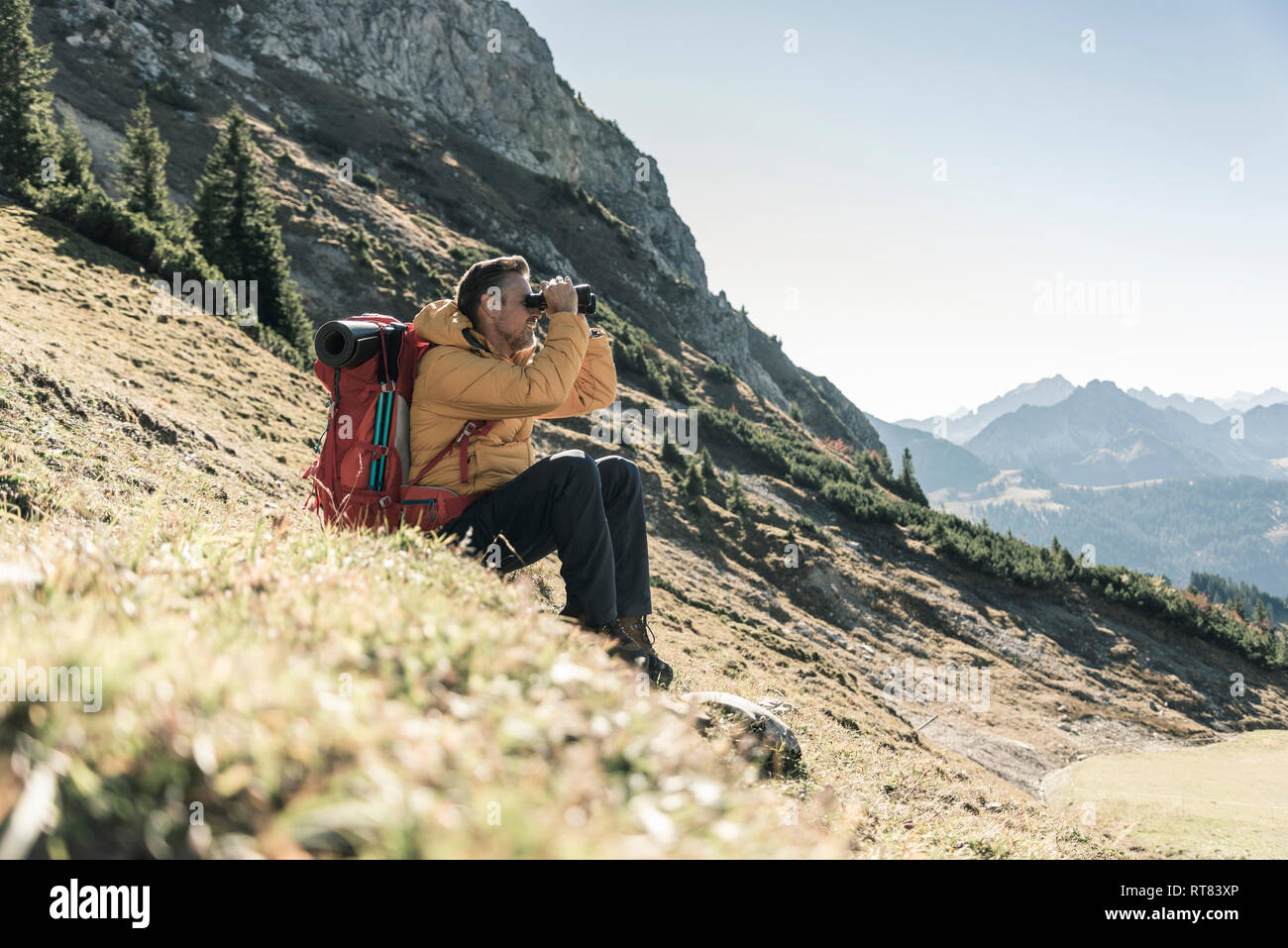 Austria, Tyrol, man having a break during a hiking trip in the mountains looking through binoculars Stock Photo
