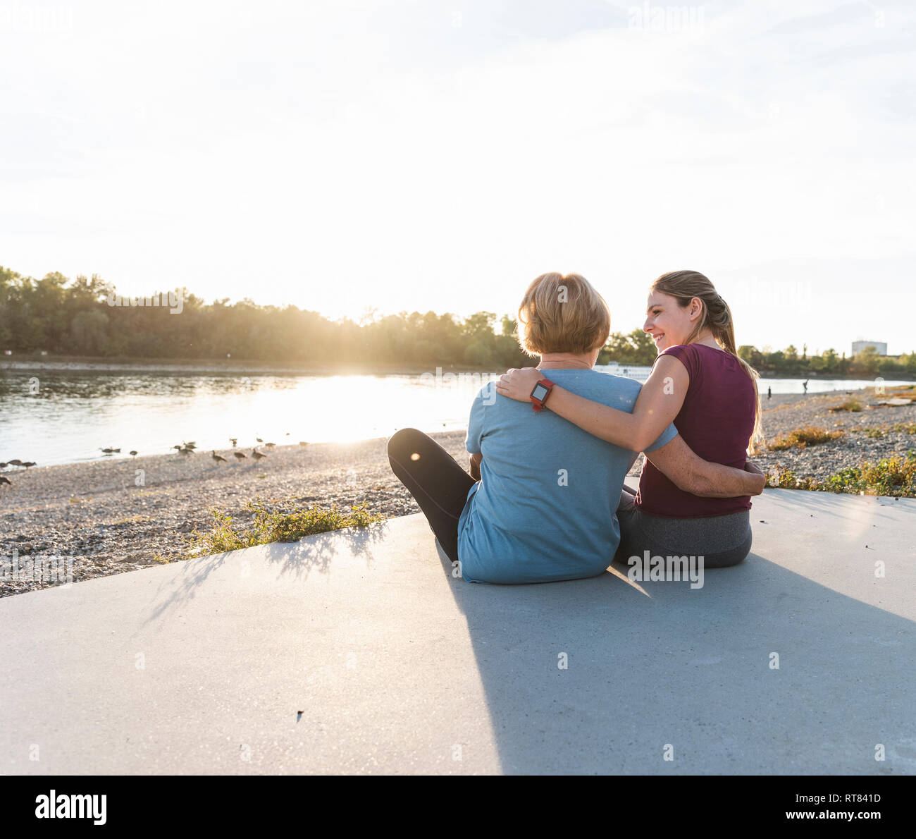 Grandmother and granddaughter sitting at the river after training, watching the sunset Stock Photo