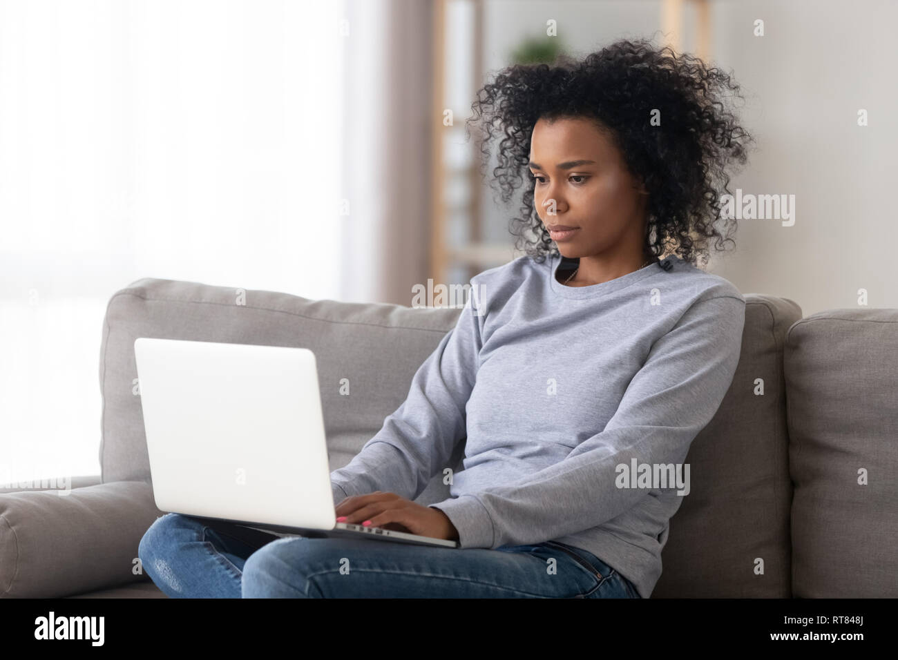 African female sitting on couch working on computer at home Stock Photo ...