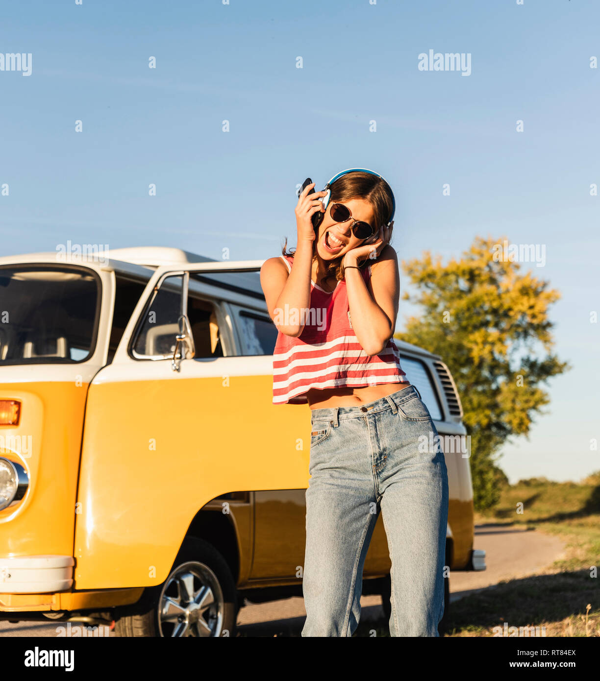 Pretty woman on a road trip with her camper, dancing, listening music ...