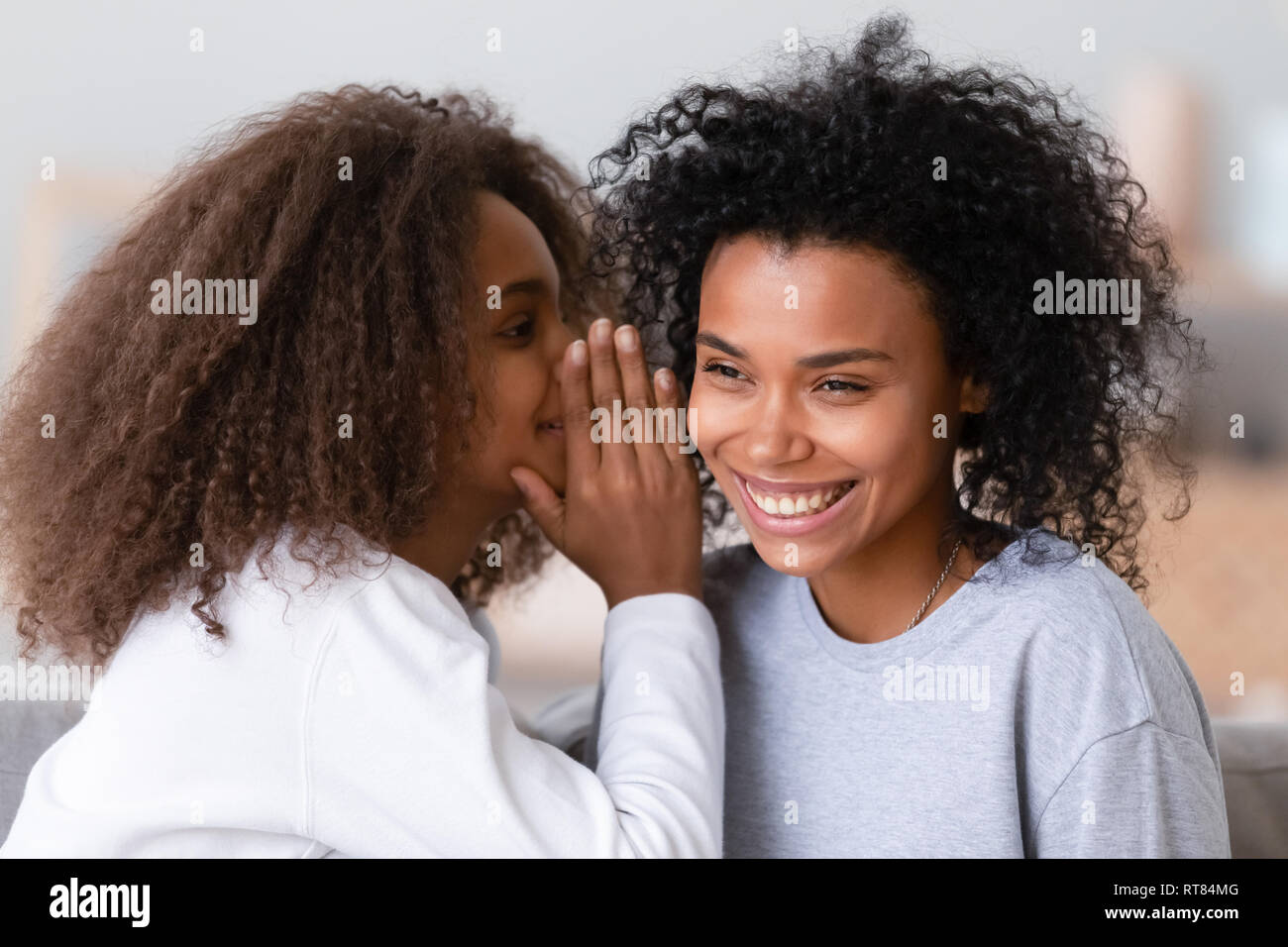Cheerful african daughter whisper to mothers ear a secret Stock Photo