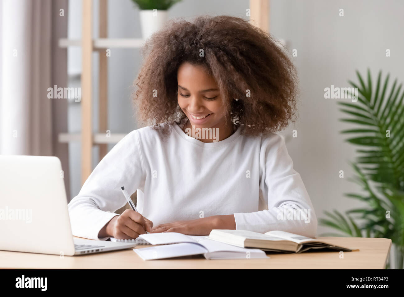 Positive african schoolgirl sitting at desk and study Stock Photo - Alamy