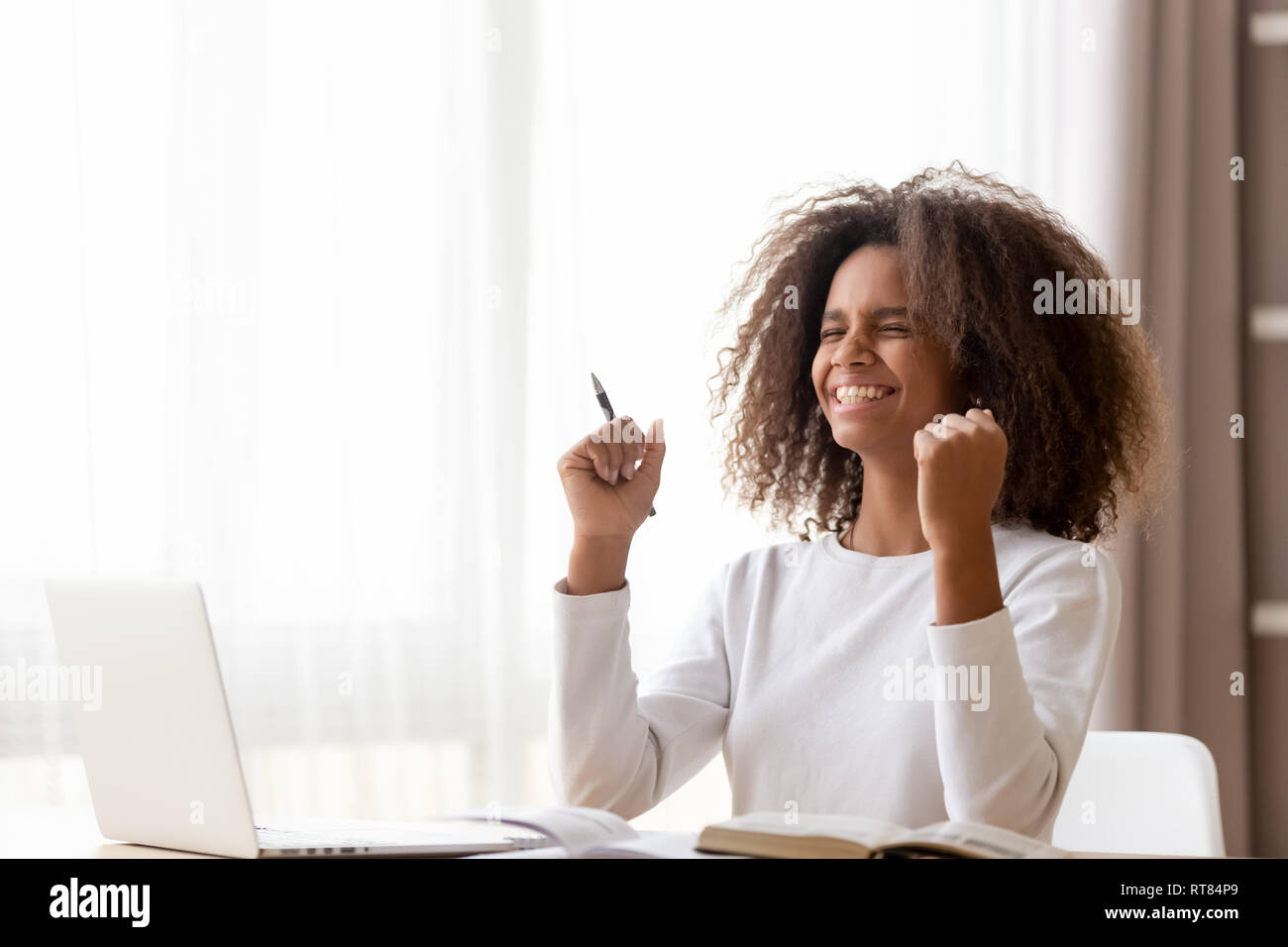 African schoolgirl sitting at desk feels happy received great news Stock Photo