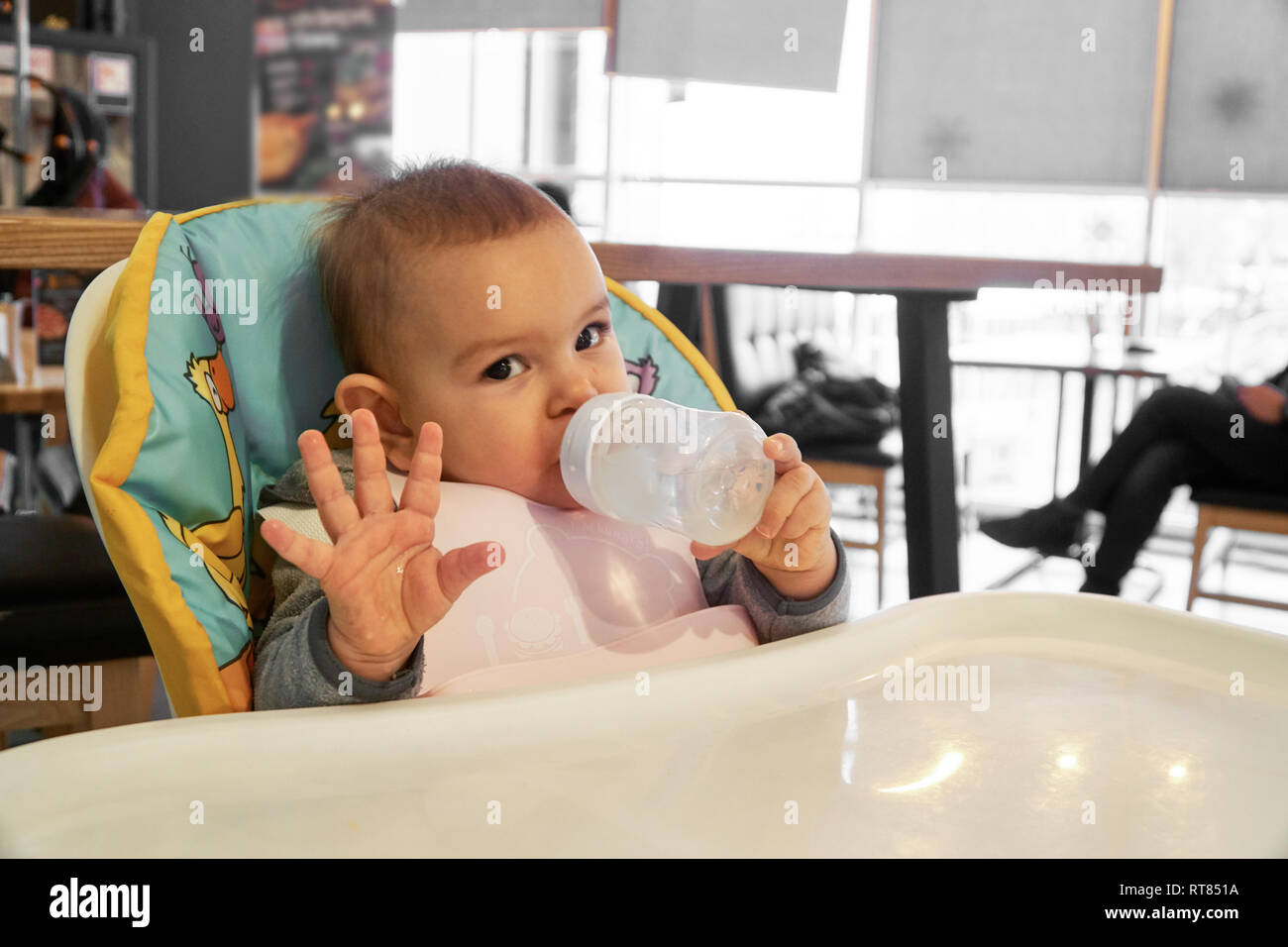 Little Baby Drinking Water From Bottle Indoors In The Cafe Or