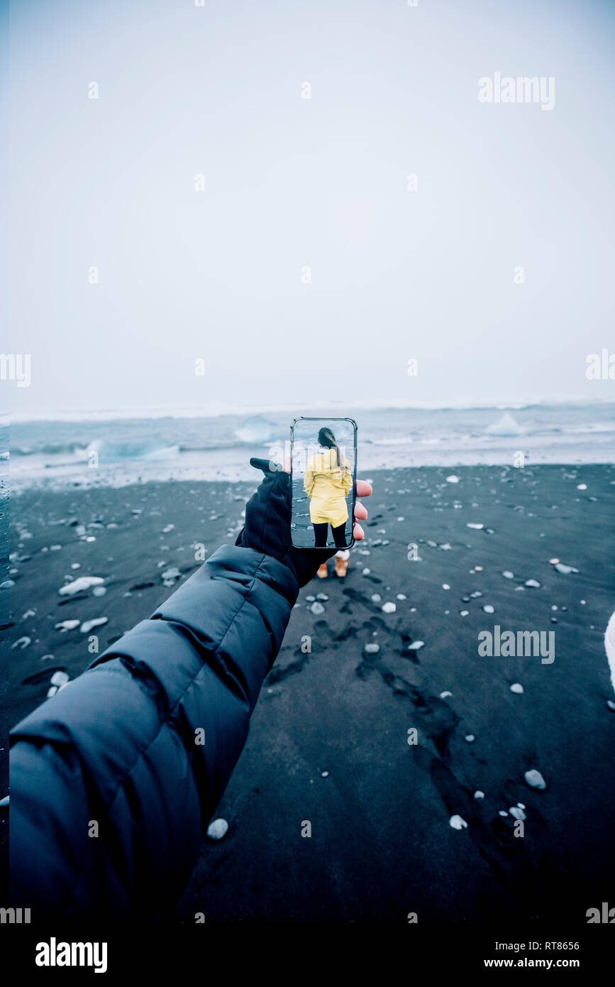 3D montage of man taking smartphone picture of Iceland's landscape and woman wearing yellow raincoat Stock Photo