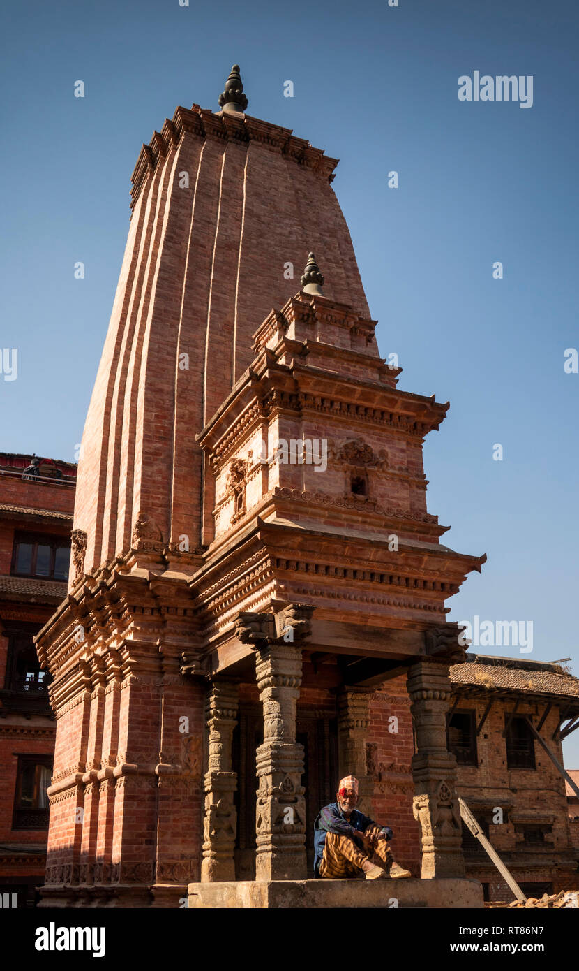 Nepal, Kathmandu Valley, Bhaktapur, Durbar Square, Kedarnath Shiva Temple, reconstructed after 2015 earthquake, man sat in shade of entrance Stock Photo