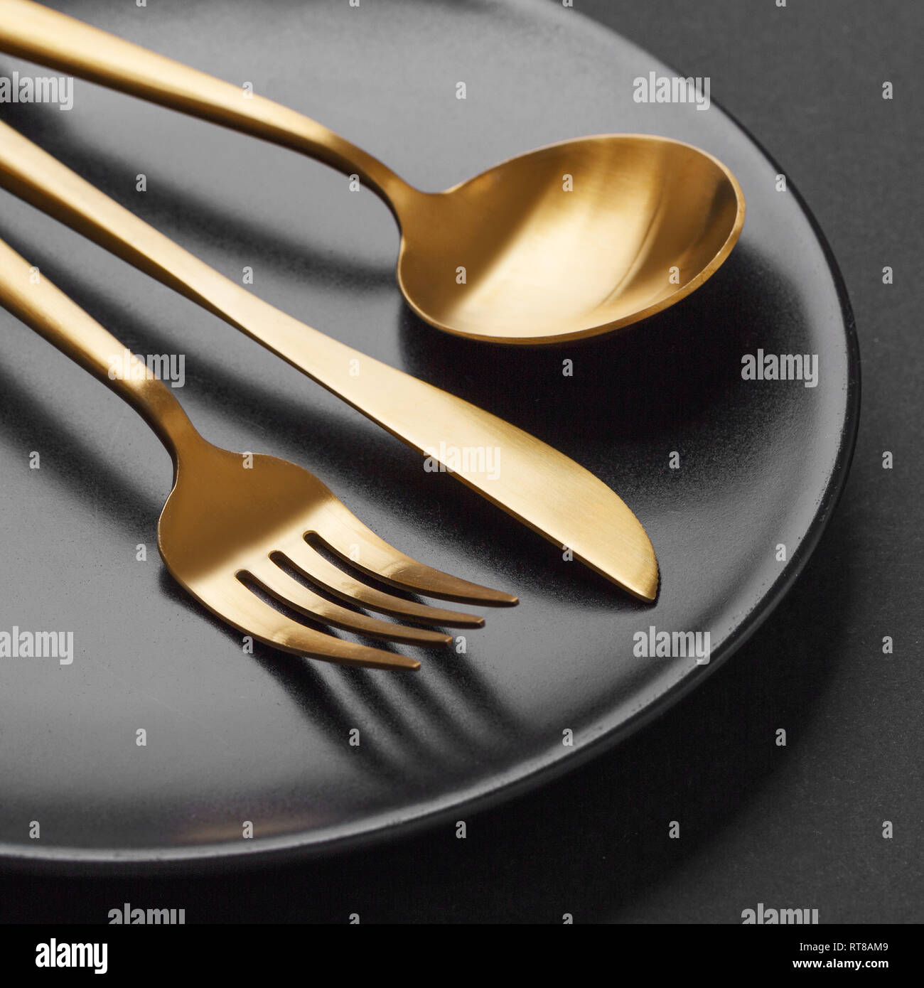 Beautiful gold cutlery fork, knife, spoon on black plate on black
