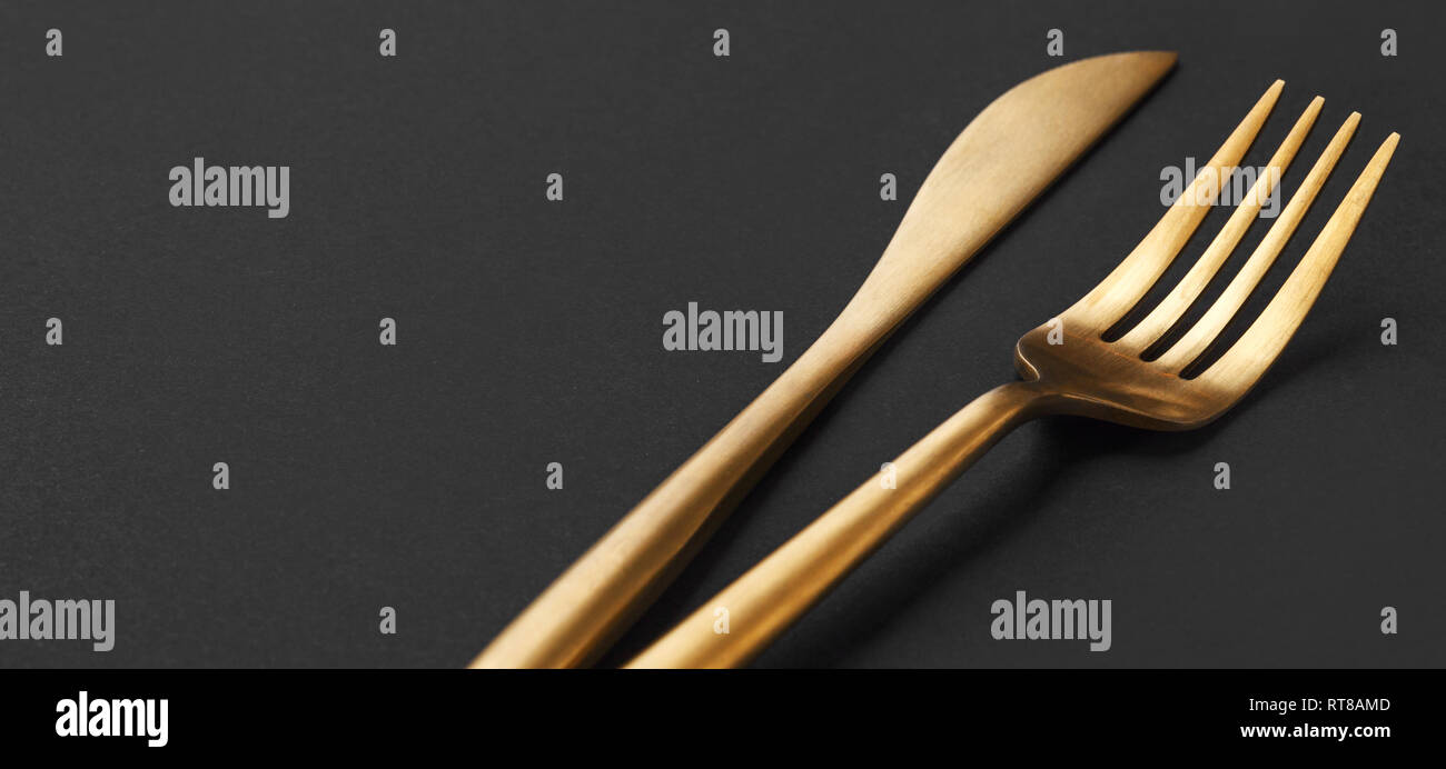 Beautiful gold cutlery fork and knife on black plate on black