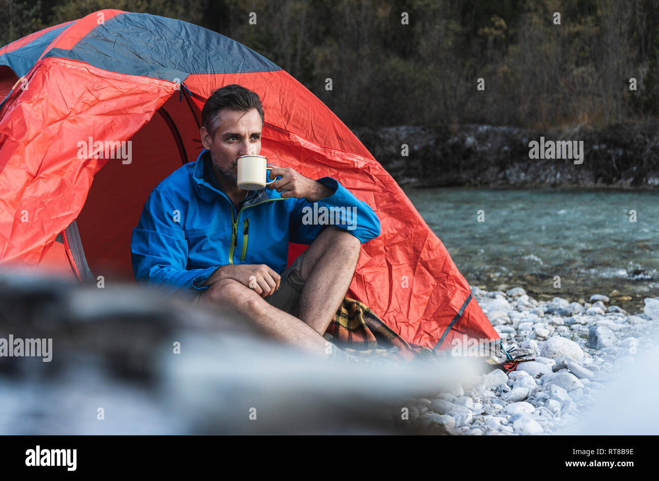 Mature man camping at riverside, drinking Stock Photo