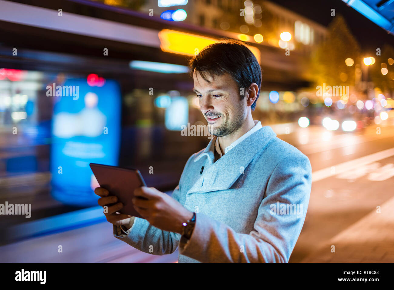Businessman with digital tablet standing at a bus stop at night Stock Photo