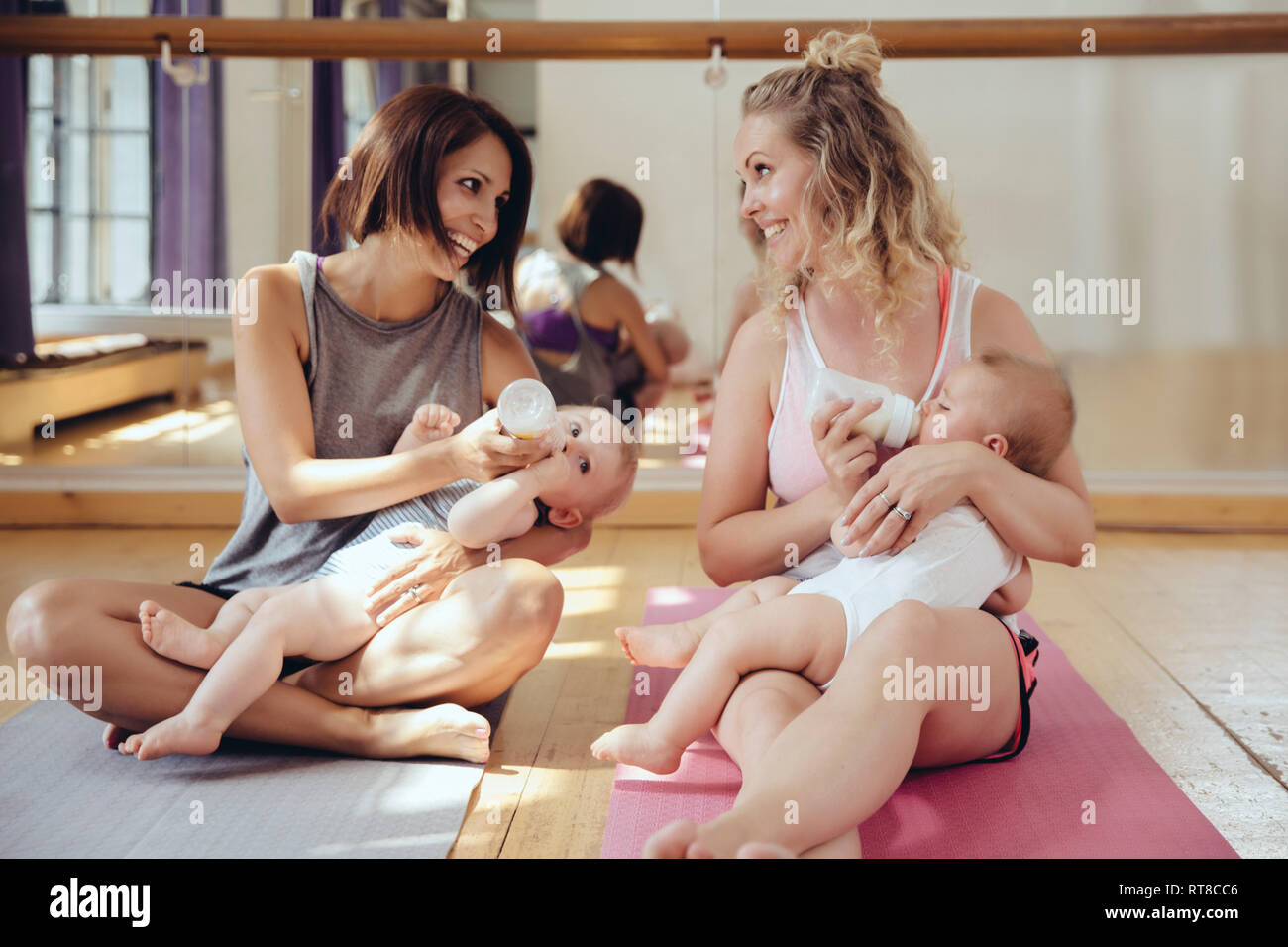 Two mothers bottle-feeding their babies in exercise room Stock Photo