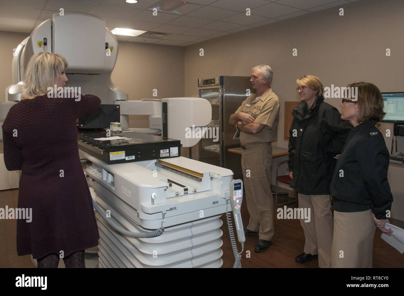 Portsmouth, Va. Kristie Ledman, a radiation therapist in Naval Medical Center Portsmouth’s (NMCP) Radiation Oncology Division, demonstrates operation of the TrueBeam linear accelerator to Capt. Christopher Culp, NMCP’s commanding officer; Rear Adm. Anne Swap, commander, Navy Medicine East; and Capt. Carolyn Rice, NMCP’s executive officer. The Radiation Oncology Division debuted a new Varian TrueBeam linear accelerator during the Jan. 25 open house and held a ribbon cutting for the $4.5-million machine that is revolutionary in the way it treats cancerous and benign tumors. Stock Photo