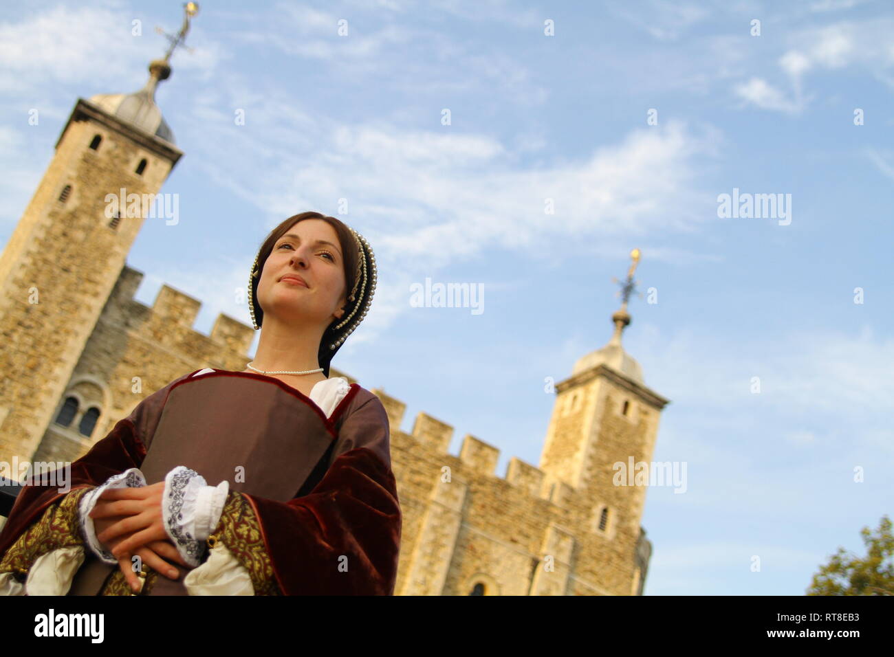 A woman dressed as Anne Boleyn stands in front of the Tower of London- she is a beautiful modern day woman in authentic dress Stock Photo
