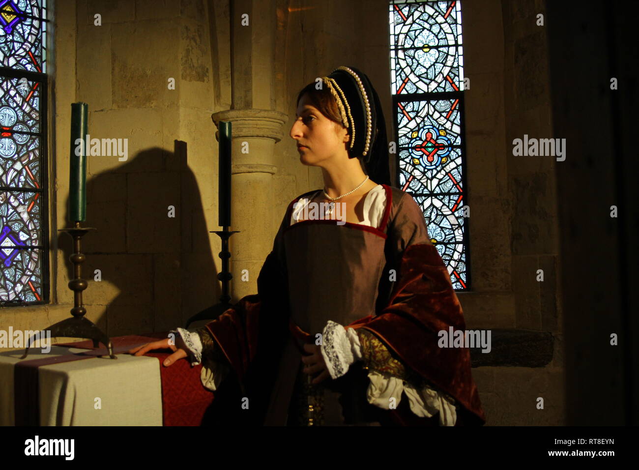 A beautiful young Woman dressed as Anne Boleyn sits by a window at the Tower of London and looks thoughtful. Stock Photo
