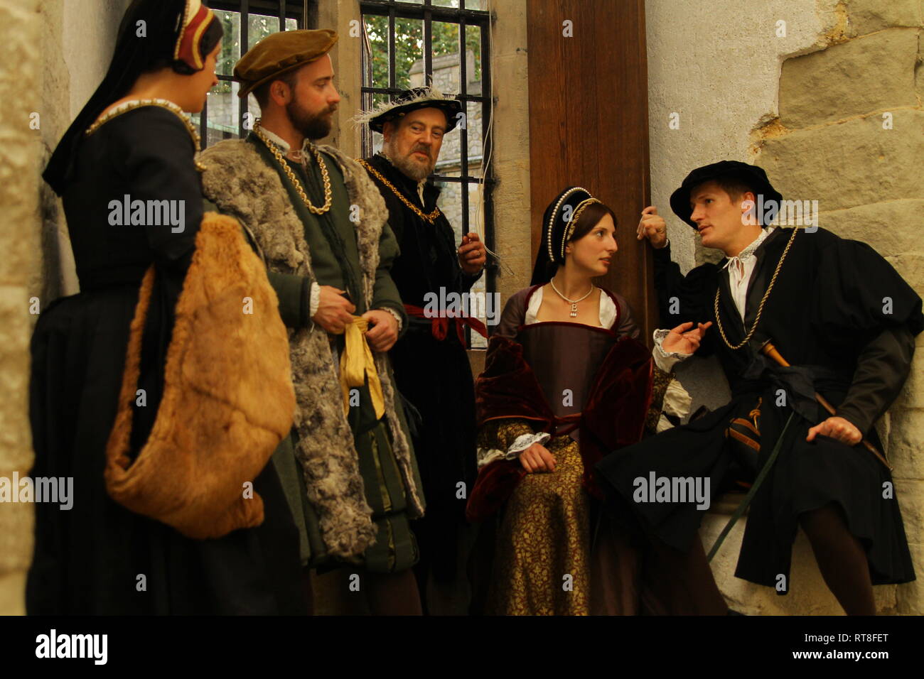 Henry VIII and Anne Boleyn with their advisors sit in a window seat at The Tower and have a conversation- they are dressed authentically Stock Photo