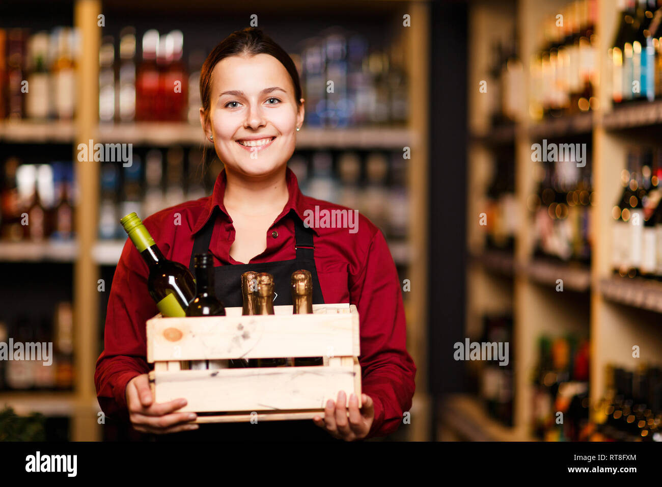 Picture of happy woman with wooden box with bottles in her hands in wine shop Stock Photo