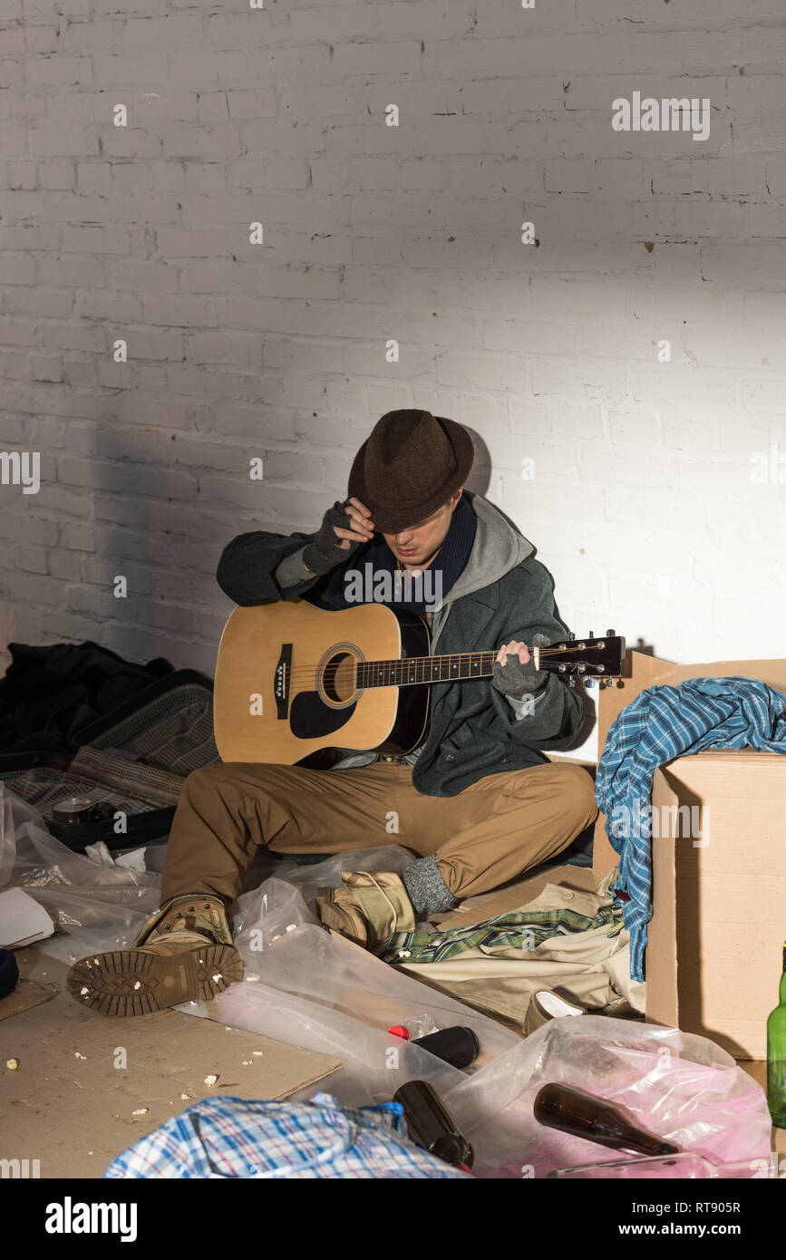 homeless man in hat and fingerless gloves holding guitar while sitting ...