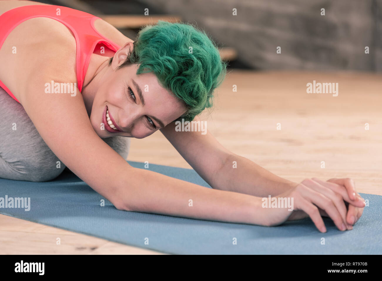 Green-eyed woman smiling while doing stretching in the gym Stock Photo