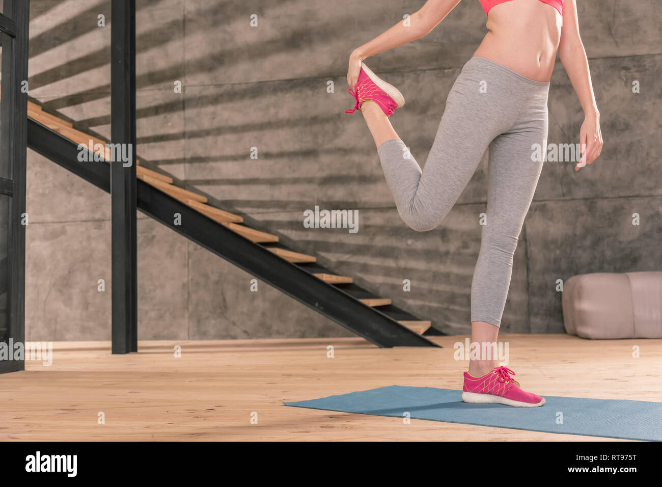 Sportswoman standing on blue mat and stretching legs after workout Stock Photo