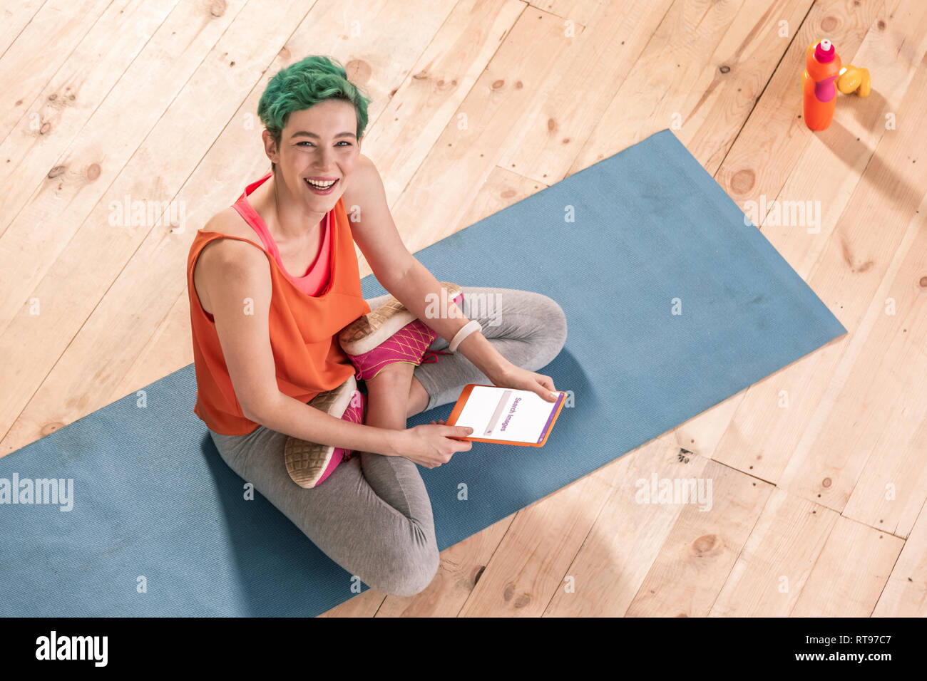 Beaming freelancer sitting with legs crossed on blue sport mat Stock Photo