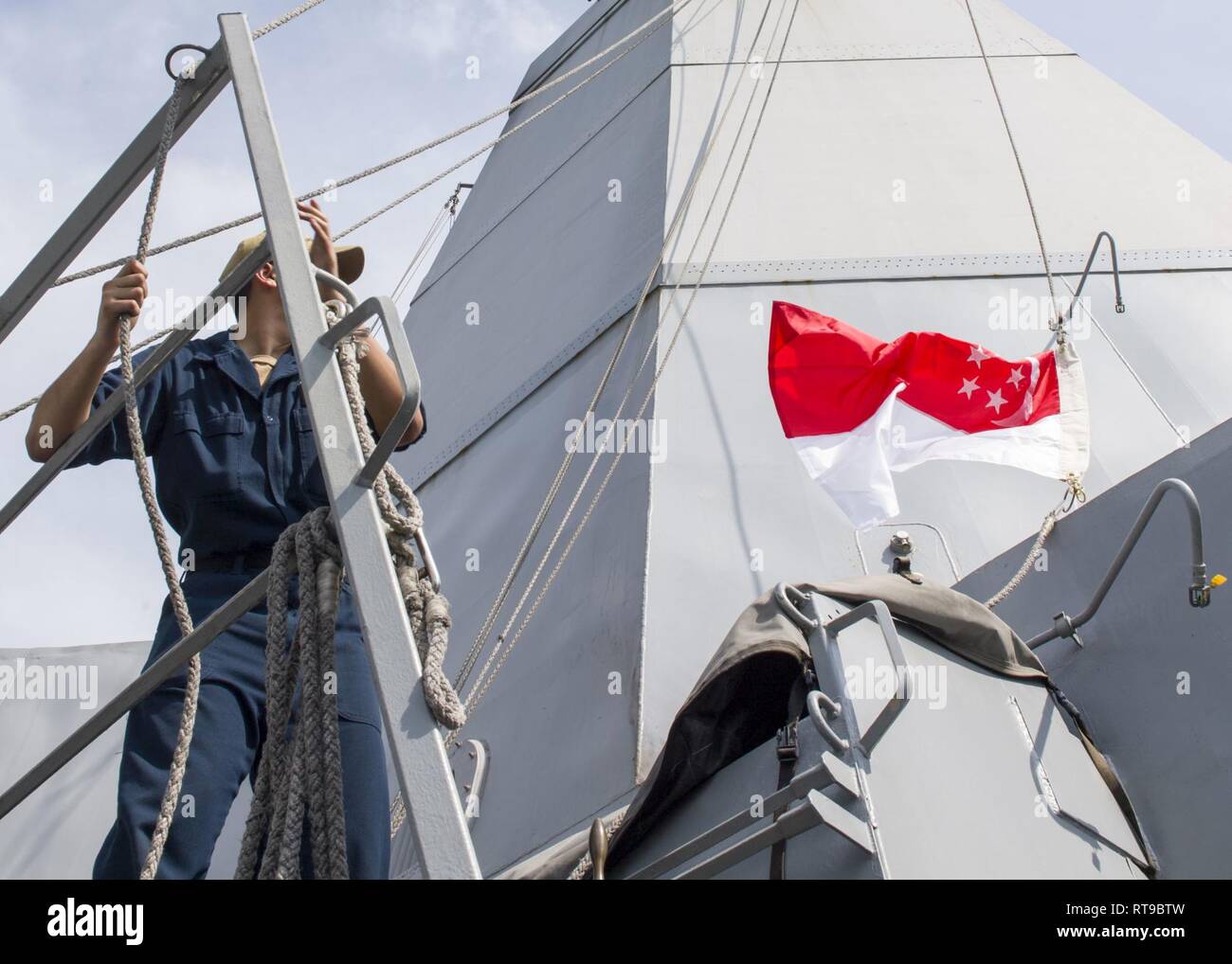 SINGAPORE (Jan. 26, 2019) Quartermaster Seaman Cesar Vallejauregui, from San Diego, raises the Singapore national flag aboard the San Antonio-class amphibious transport dock ship USS Anchorage (LPD 23) during a port visit to Singapore while on a deployment of the Essex Amphibious Ready Group (ARG) and 13th Marine Expeditionary Unit (MEU). The Essex ARG/ 13th MEU is a capable and lethal Navy-Marine Corps team deployed to the 7th fleet area of operations to support regional stability, reassure partners and allies and maintain a presence postured to respond to any crisis ranging from humanitarian Stock Photo