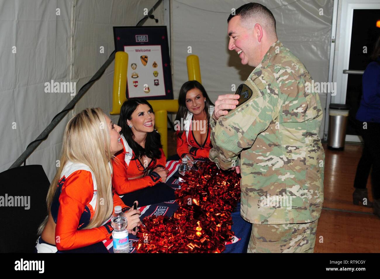U.S. Army Chief Warrant Officer 3 Michael Hamilton assigned to the 1st Armored Brigade Combat Team, 1st Cavalry Division chats with cheerleaders about his 1st Cavalry patch as part of a USO meet and greet with the Denver Broncos cheerleaders, mascot and Alumni football players at Camp Aachen's USO annex in Grafenwoehr, Germany, Jan. 26, 2019. IRONHORSE deployed in support of Atlantic Resolve, an enduring exercise to improve interoperability between U.S. Forces, their NATO allies and partners. Stock Photo