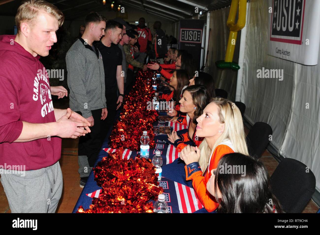 U.S. Army Spc. Jordan Vishneski, far left, assigned to 91st Brigade Engineer Battalion, 1st Armored Brigade Combat Team, 1st Cavalry Division chats with cheerleaders as part of a USO meet and greet with the Denver Broncos cheerleaders, mascot and Alumni football players at Camp Aachen's USO annex in Grafenwoehr, Germany, Jan. 26, 2019.   IRONHORSE deployed in support of Atlantic Resolve, an enduring exercise to improve interoperability between U.S. Forces, their NATO allies and partners. Stock Photo