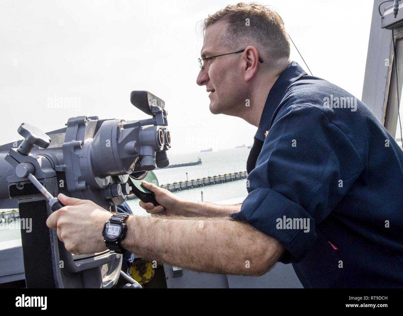SINGAPORE (Jan. 26, 2019) Lt. Cmdr. Christopher McCurry, executive officer of the San Antonio-class amphibious transport dock ship USS Anchorage (LPD 23), uses the “big eye” binoculars during a sea and anchor detail while on a deployment of the Essex Amphibious Ready Group (ARG) and 13th Marine Expeditionary Unit (MEU). The Essex ARG/13th MEU is a capable and lethal Navy-Marine Corps team deployed to the 7th fleet area of operations to support regional stability, reassure partners and allies and maintain a presence postured to respond to any crisis ranging from humanitarian assistance to conti Stock Photo