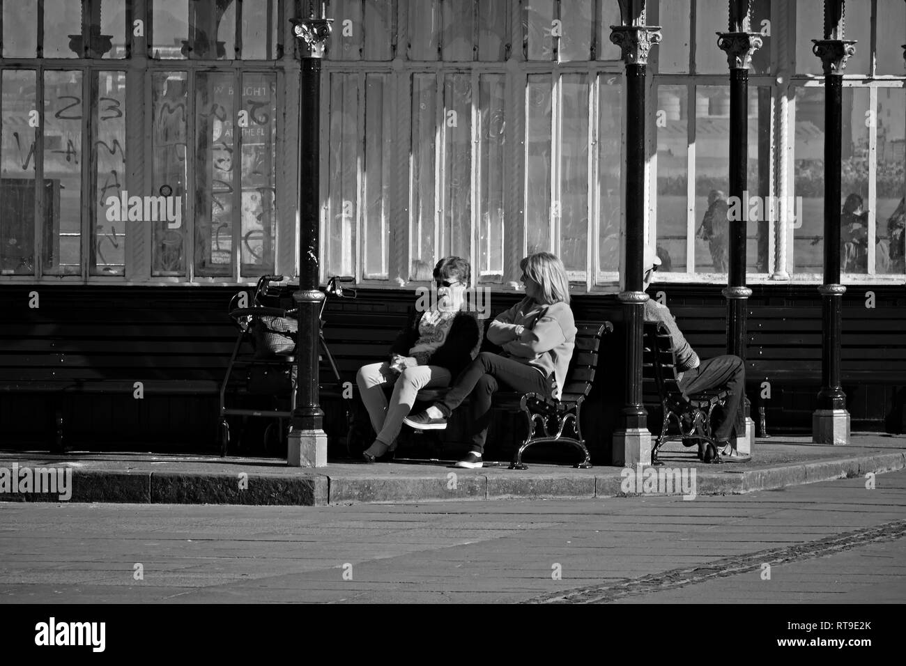 Monochrome image of 2 women sitting on a bench in a Victorian shelter at New Brighton Merseyside UK. Stock Photo
