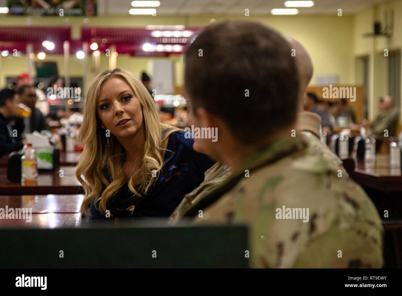 Haley, a Denver Broncos cheerleader, talks with Soldiers from the 4th Combat Aviation Brigade, 4th Infantry Division, in the Flight Line Cafe Dining Facility as part of the Denver Broncos Pro Blitz Tour sponsored by Armed Forces Entertainment in Illesheim, Germany, Jan. 28, 2019.    The Denver Broncos Pro Blitz Tour featuring the Denver Broncos Cheerleaders, Miles the team mascot and former players, is orchestrated by Armed Forces Entertainment in order to provide the best unique entertainment to U.S. troops and family members stationed overseas. Stock Photo