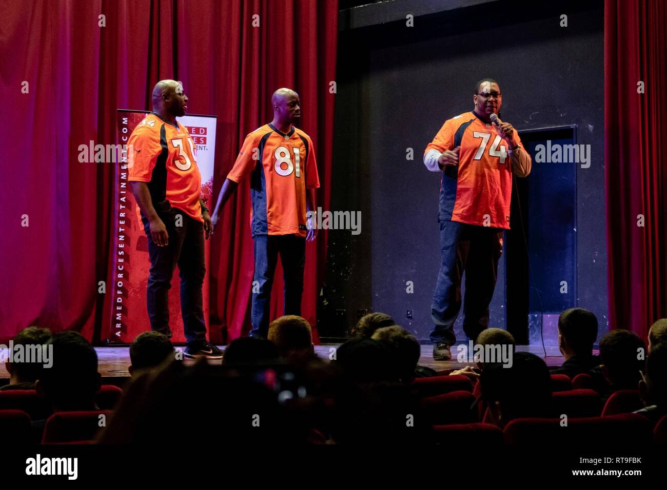 Reuben Droughns III, Charles Adams and Orlando Franklin, from right, former players for the Denver Broncos football team, address Soldiers from the 4th Combat Aviation Brigade, 4th Infantry Division, operating out of Ft. Carson, Colo., during the Denver Broncos Pro Blitz Tour at the theater in Illesheim, Germany, Jan. 28, 2019.    The Denver Broncos Pro Blitz tour, coordinated by Armed Forces Entertainment, provided a unique opportunity or members of 4th CAB to meet and interact with former players, the cheerleading team and the mascot of their hometown Denver Broncos. Stock Photo