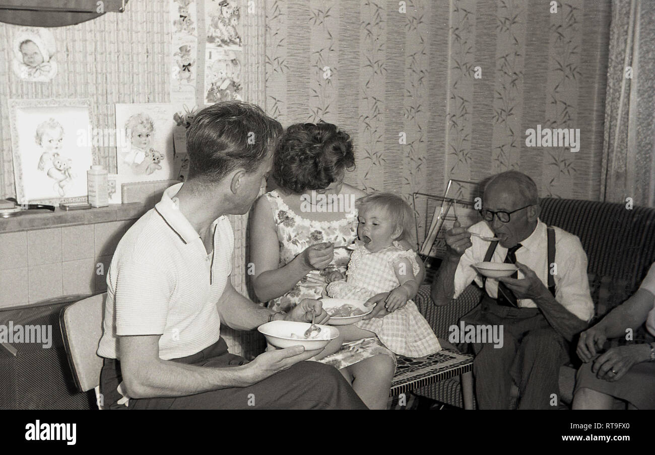1950s, historical, Family life, different generations of a family sitting together in a front room eating a pudding, with mother feeding her infant daughter, England, UK. Stock Photo