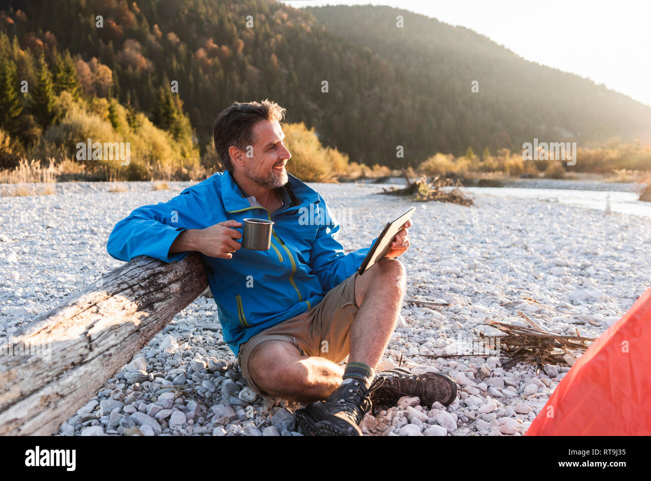 Mature man camping at riverside, using tablet Stock Photo
