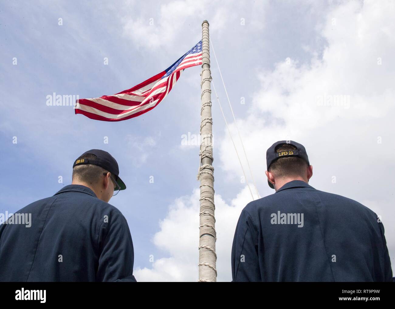 SINGAPORE (Jan. 31, 2019) Aviation Support Equipment Technician 2nd Class Salam Sabah, from Detroit, left, and Aviation Boatswain’s Mate (Fuel) 3rd Class Dylan Wilson, from Hawkins, Texas, prepare to lower the American flag aboard the San Antonio-class amphibious transport dock ship USS Anchorage (LPD 23) while on a deployment of the Essex Amphibious Ready Group (ARG) and 13th Marine Expeditionary Unit (MEU). The Essex ARG/13th MEU is a capable and lethal Navy-Marine Corps team deployed to the 7th fleet area of operations to support regional stability, reassure partners and allies and maintain Stock Photo