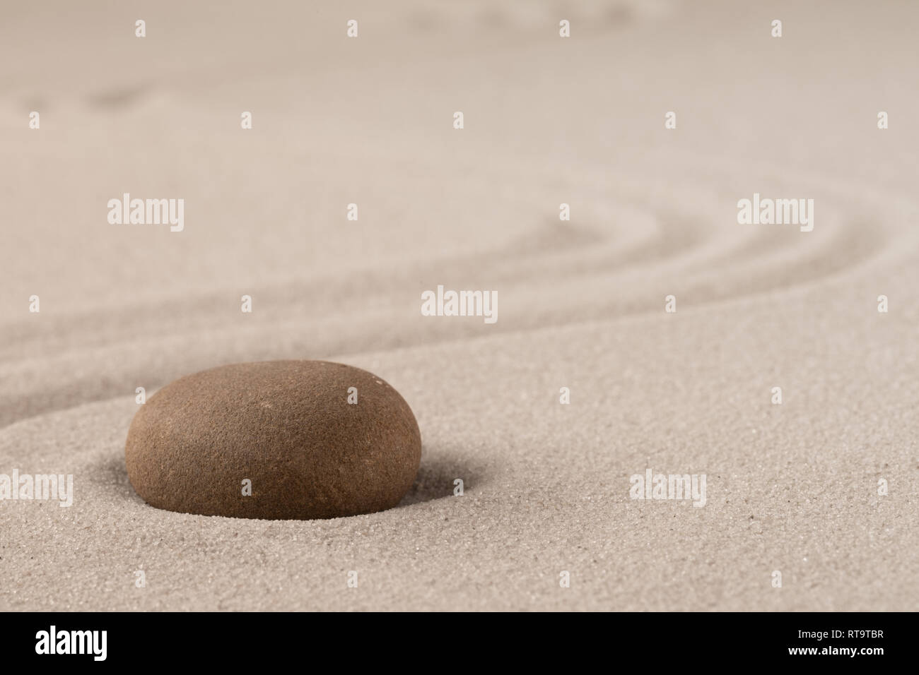 Concentration trough focus on a zen meditation stone. Round rock in sand texture background. Concept for yoga or spa welness treatment. Stock Photo