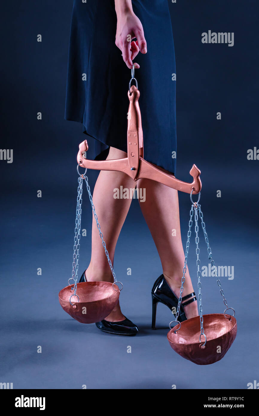 The graceful legs of a young girl and her hand holding Libra, as a symbol of the air sign of the zodiac. Dark background Stock Photo