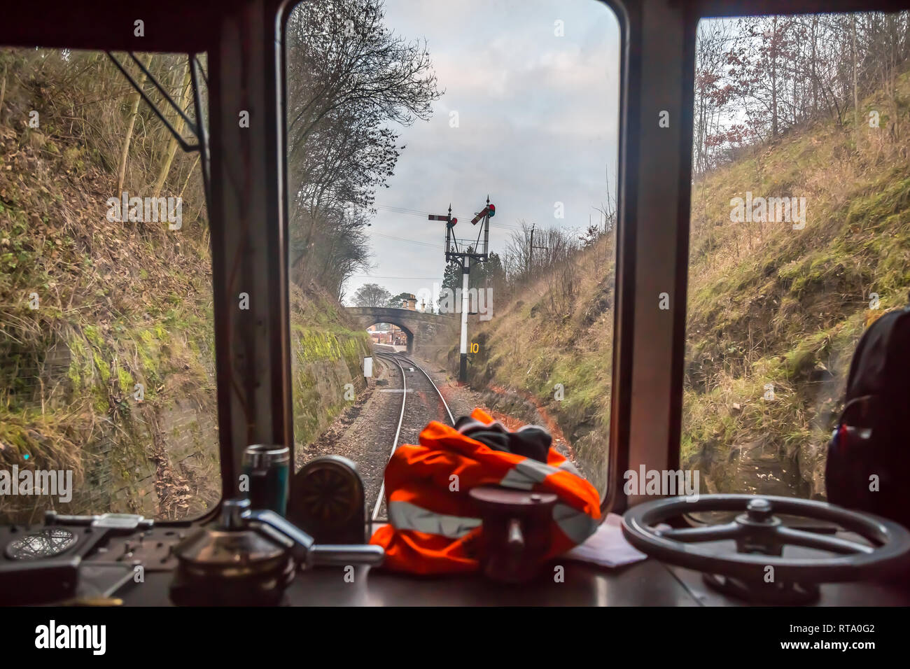 Diesel train driver's cockpit view of track & signals through window of moving train on Severn Valley Railway, approaching Arley vintage train station. Stock Photo