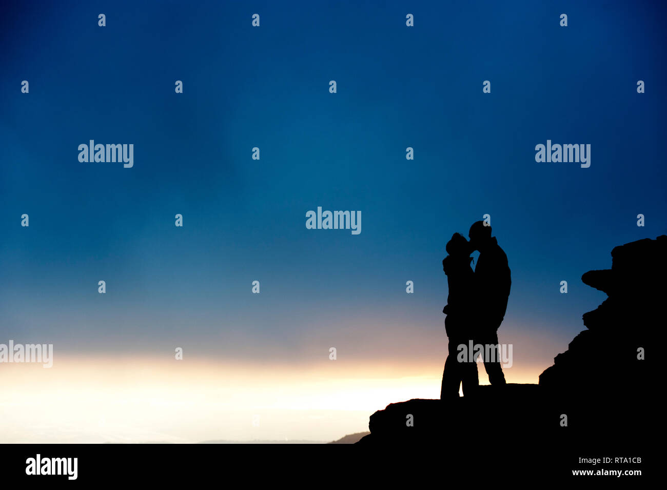 silhouette of couple of man and woman kissing on a mountain with storm background Stock Photo