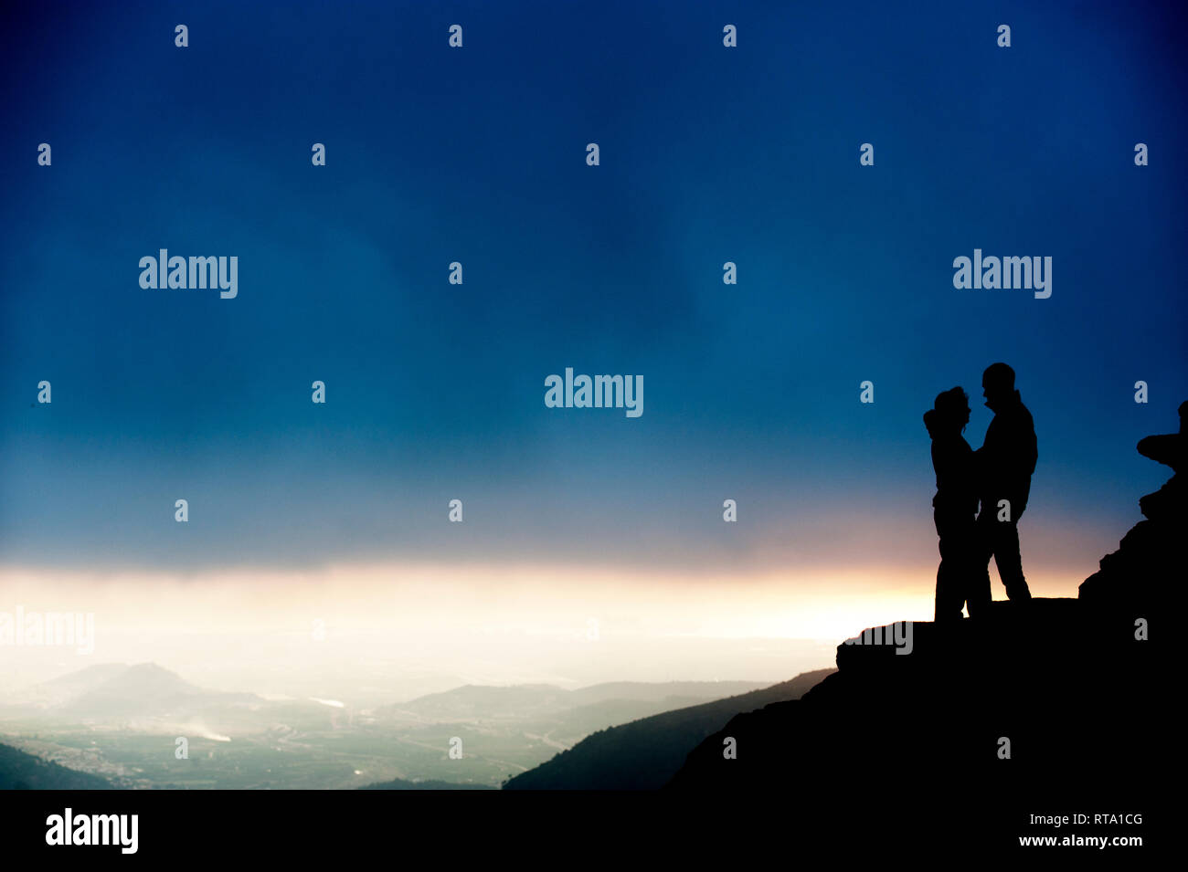 silhouette of couple of man and woman on a mountain with storm background Stock Photo