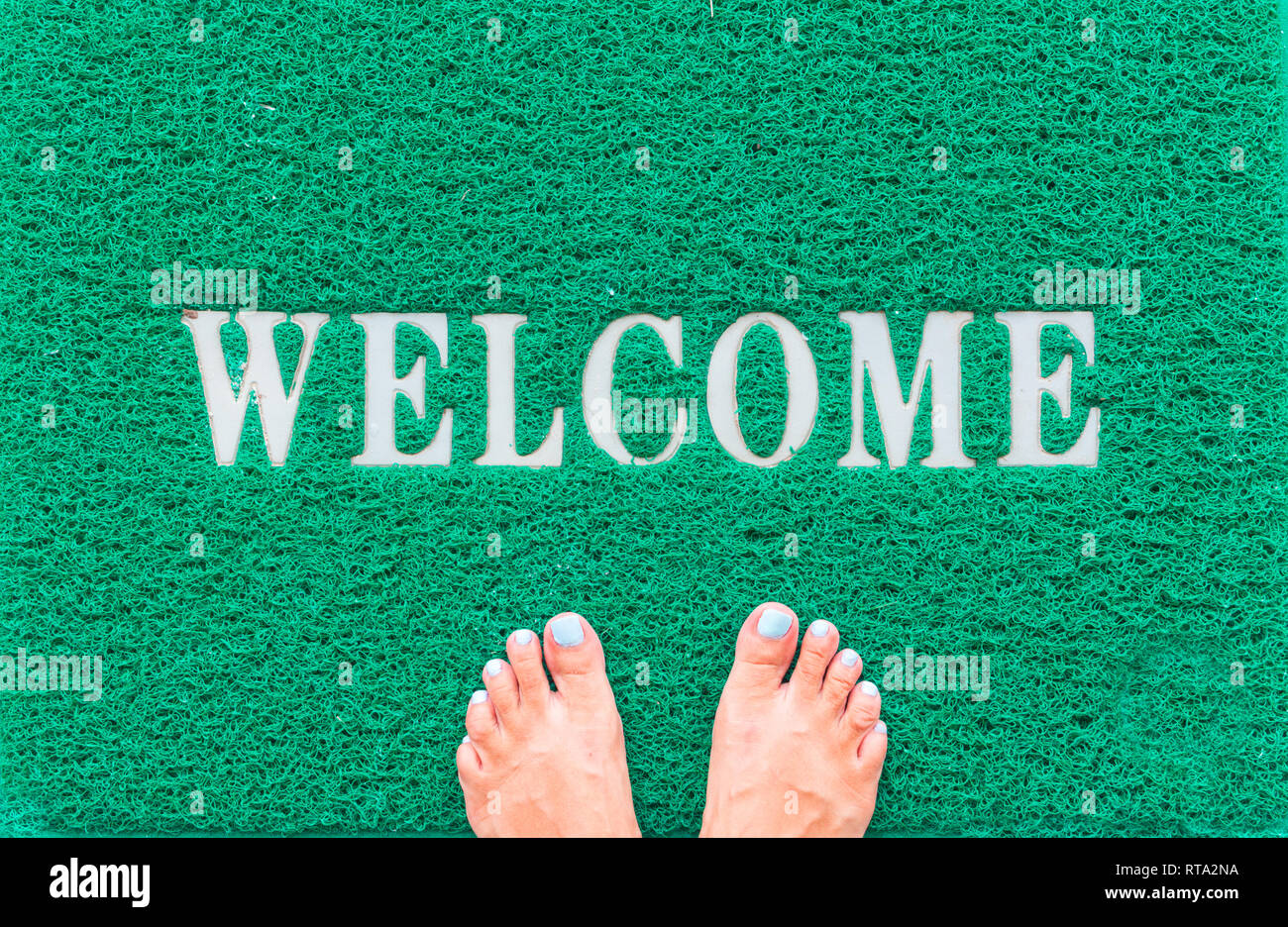 green foot scraper mat on wooden floor with barefoot standing Stock