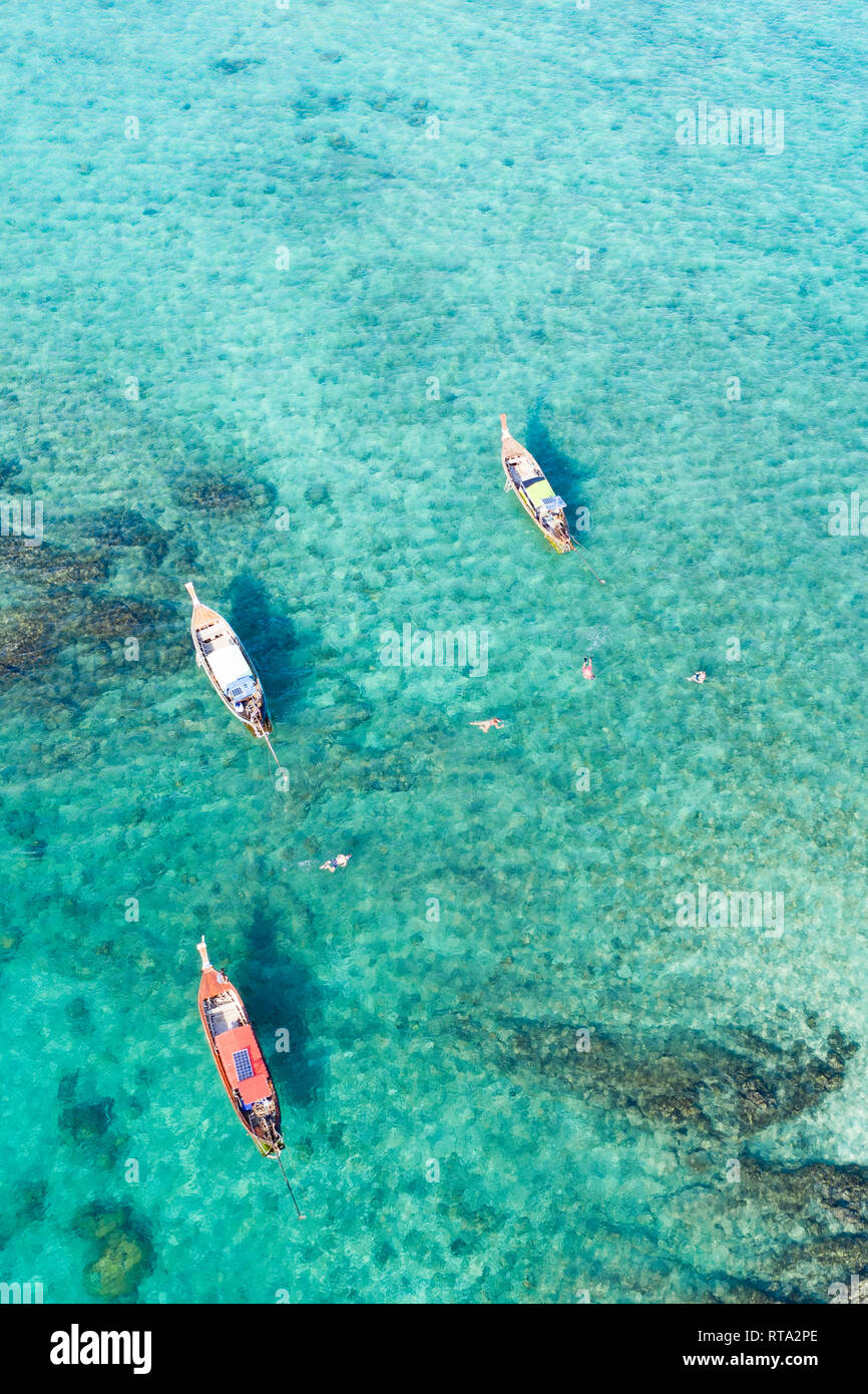 View from above, stunning aerial view of some long-tails boats and tourists who do snorkeling in a beautiful, transparent and turquoise sea. Stock Photo