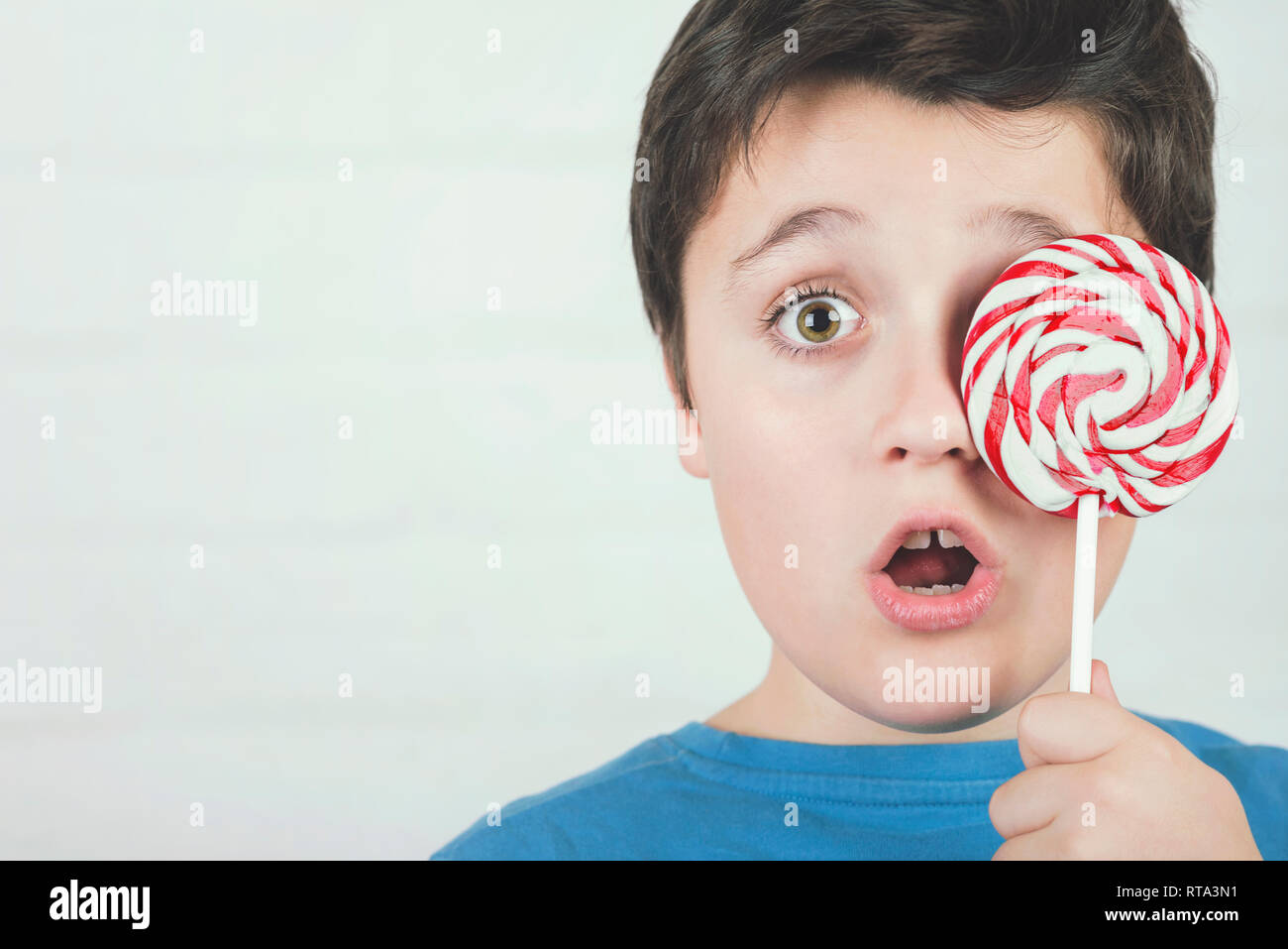 Portrait of child covering eye with lollipop against brick background Stock Photo