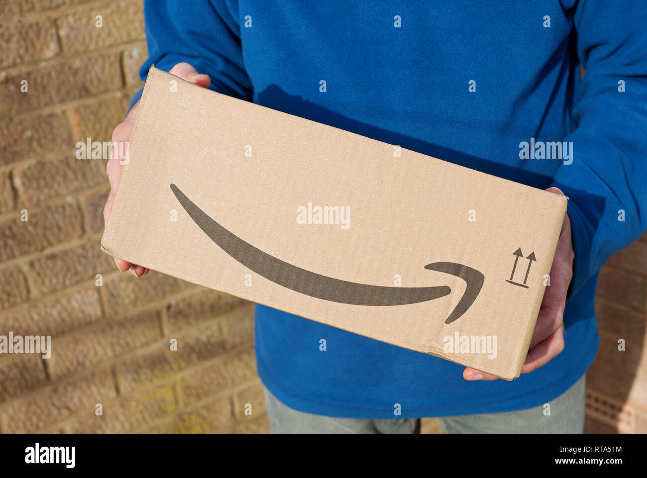 Close up of man person holding carrying Amazon box package delivery parcel home internet shopping England UK United Kingdom GB Great Britain Stock Photo
