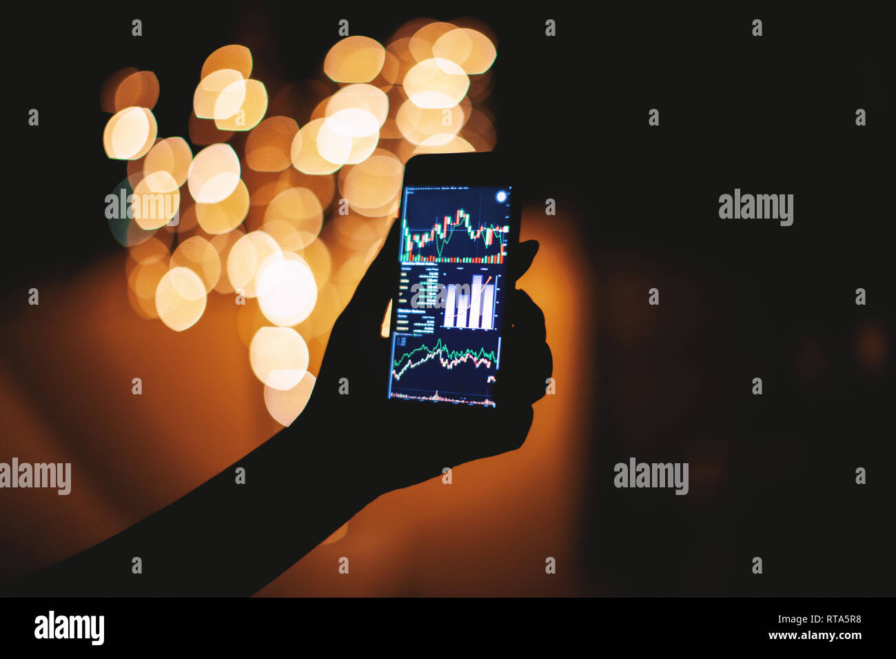 Woman hand holding mobile phone with stock trading on display in the dark with light bokeh blurry background, Financial, Commerce, Business and techno Stock Photo