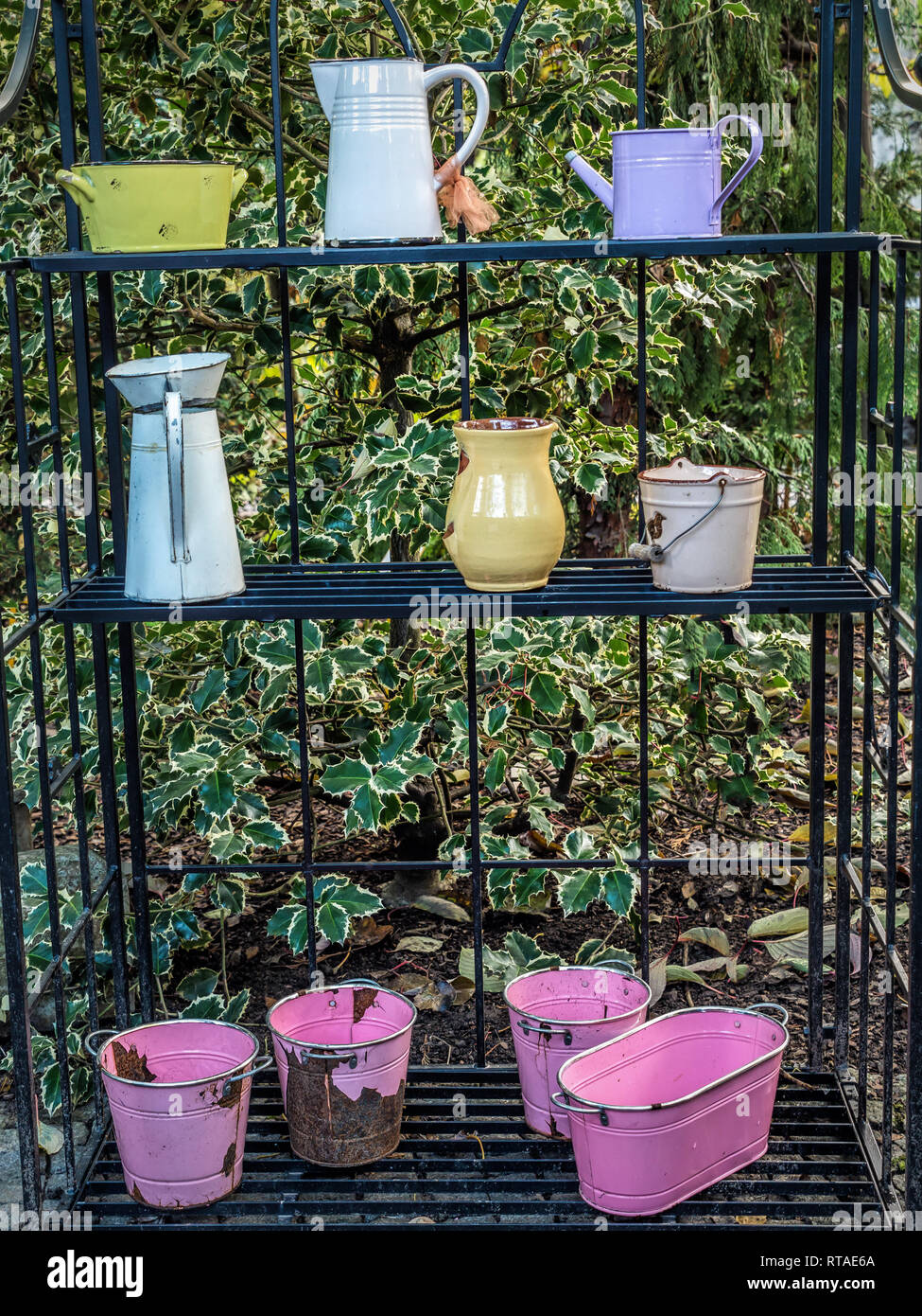 Old watering cans and other garden utensils and vessels placed outside on metal rack as decorations in the garden Stock Photo