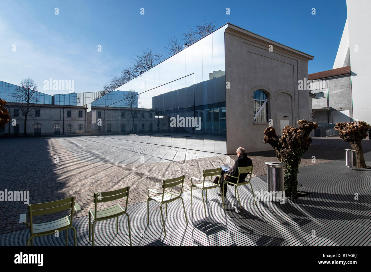 Man sitting on a chair in one of the couryards of Fondazione Prada, exterior, Milan, Italy Stock Photo